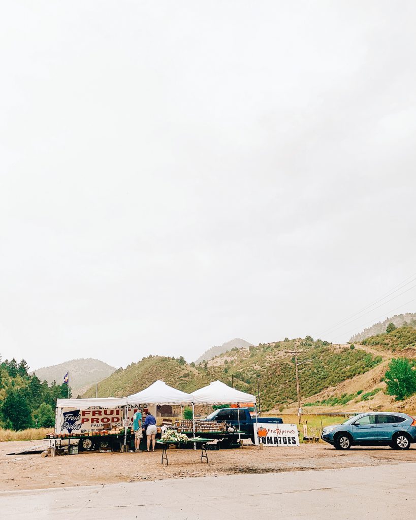 A produce stand in the rain with mountains in the background. A sign reads 'Fruit and Produce' and 'Tomatoes'. 