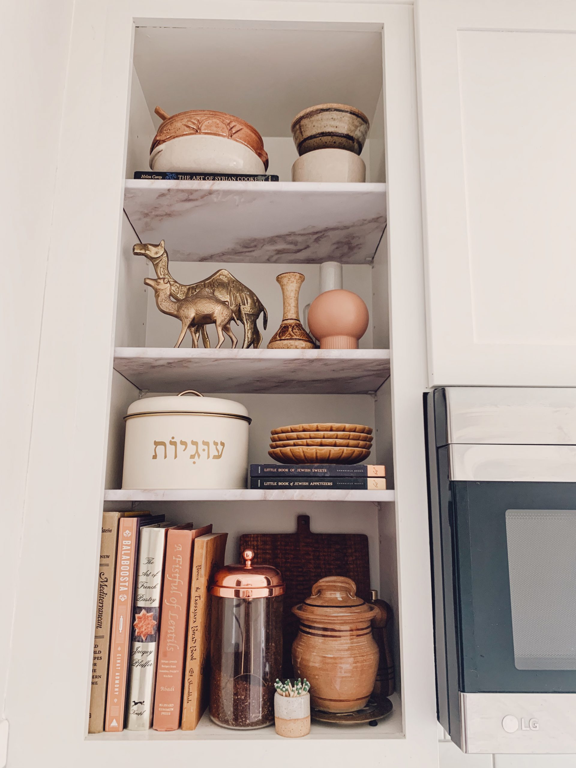 An open kitchen shelf, with faux marble contact paper shelf coverings and decor.